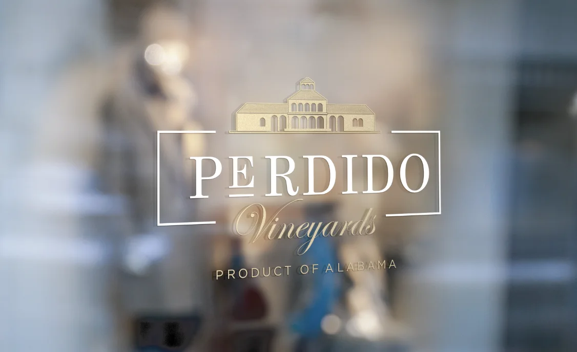 Logo Perdido Vineyards aplicado sobre el vidrio del frente de la bodega, con reflejos del interior