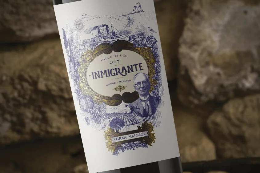 Botella El Inmigrante apoyada sobre piedra — etiqueta en azul cobalto