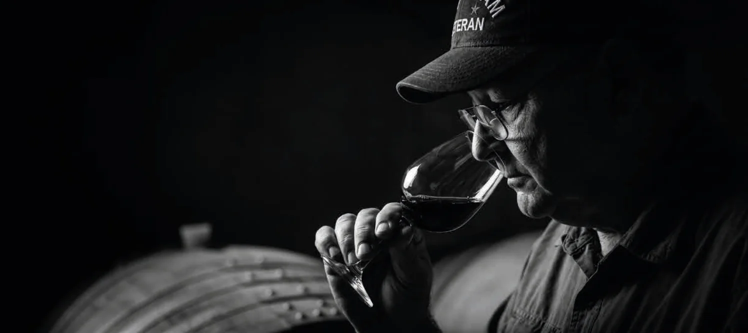 Jim Eddins evaluando el color y el cuerpo del vino frente a las barricas de roble